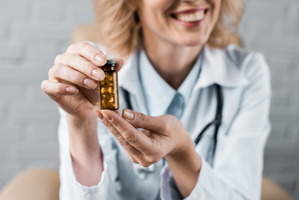 обрезанный снимок улыбающейся женщины-врача, показывающей банку с таблетками пациенту в офисе
 - Фото, изображение