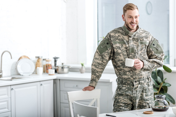 キッチンで一杯のコーヒーを保持している笑顔の陸軍兵士 - 写真・画像