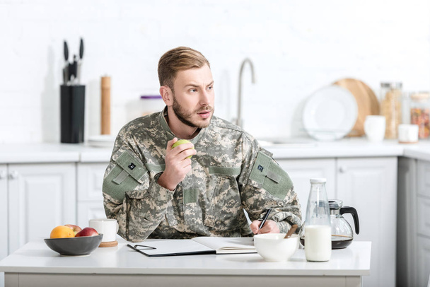 військовий солдат сидить за кухонним столом і їсть яблуко
 - Фото, зображення