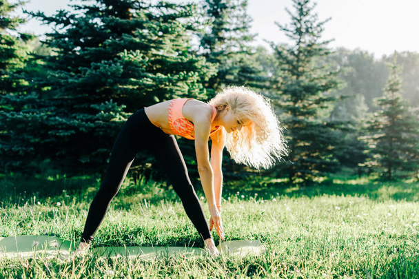 Photo of young curly-haired sports woman practicing yoga on rug  - 写真・画像