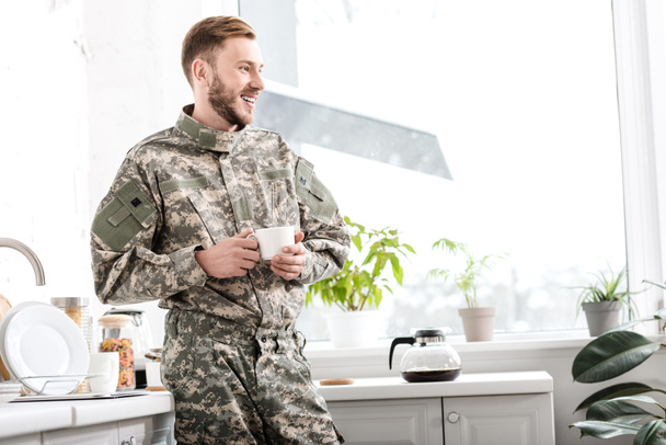 smiling army soldier holding cup of coffee in kitchen - Foto, immagini