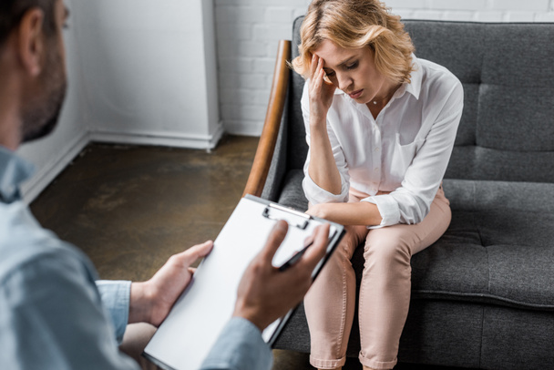 depressed woman having psychologist therapy session at office while therapist holding clipboard - Photo, Image