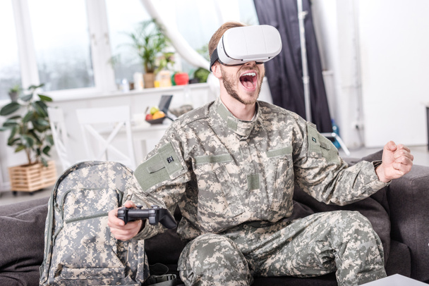 excited soldier in virtual reality headset playing video game on couch  - Фото, зображення