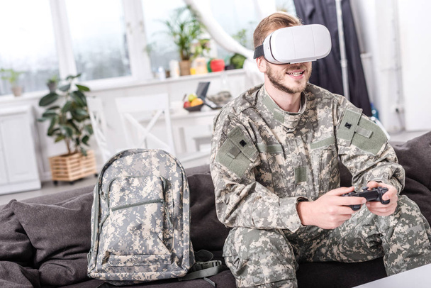 Lächelnder Soldat im Virtual-Reality-Headset beim Videospiel auf der Couch  - Foto, Bild