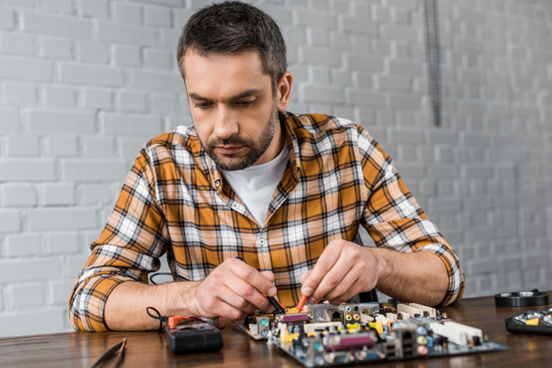 concentrated computer engineer with tester examining motherboard - Photo, Image