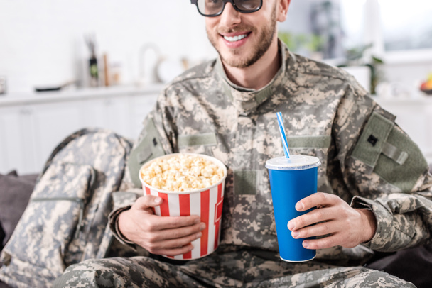улыбающийся солдат в 3D очках смотрит фильм с попкорном и газировкой
  - Фото, изображение