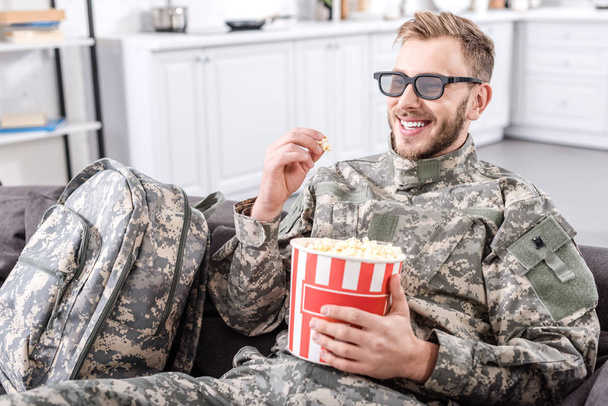 3d gözlük takan, patlamış mısır yemek ve kanepe film izlerken askeri üniformalı asker gülümseyen - Fotoğraf, Görsel