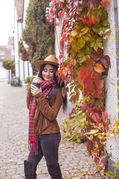 Jonge mooie Turkse vrouw loopt in een Europese stad. Een meisje heeft een glas koffie. Gelukkig brunette in een hoed. Herfst. Mode. - Foto, afbeelding