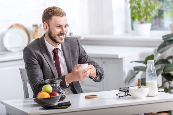 handsome businessman having breakfast and drinking coffee at kitchen table - Photo, image