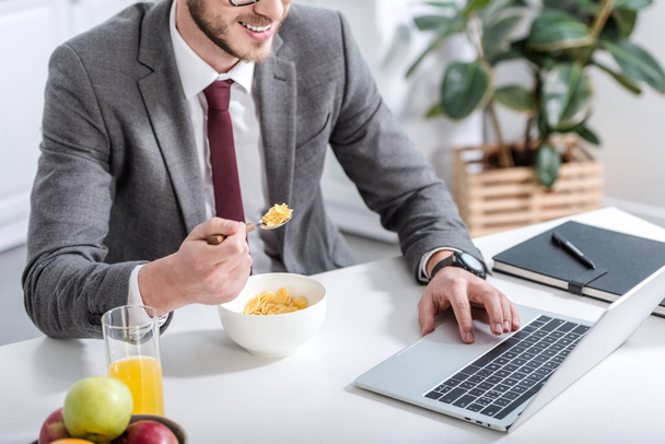 businessman working on laptop while eating breakfast at kitchen - Fotografie, Obrázek