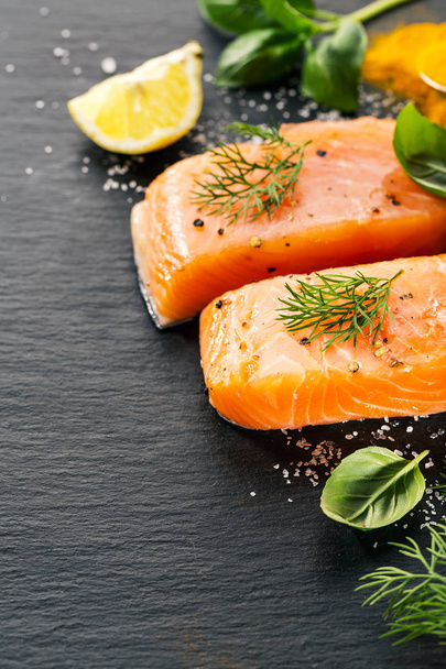 Bistecche di salmone fresche e gustose crude su tavola nera con ingredienti
 - Foto, immagini