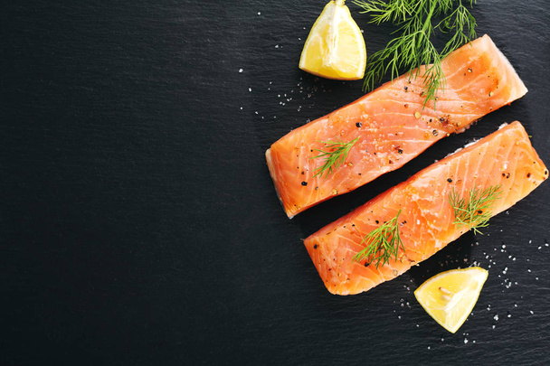 top view of Raw fresh tasty salmon steaks on black table with ingredients - Valokuva, kuva