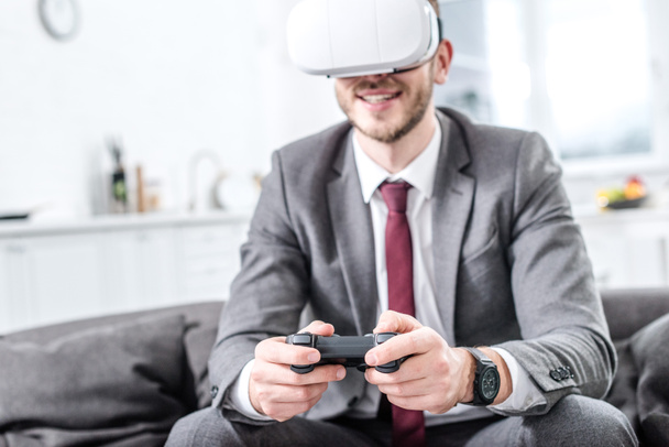 nadšený podnikatel nošení soupravu pro virtuální realitu a hrát videohry na gauči doma - Fotografie, Obrázek