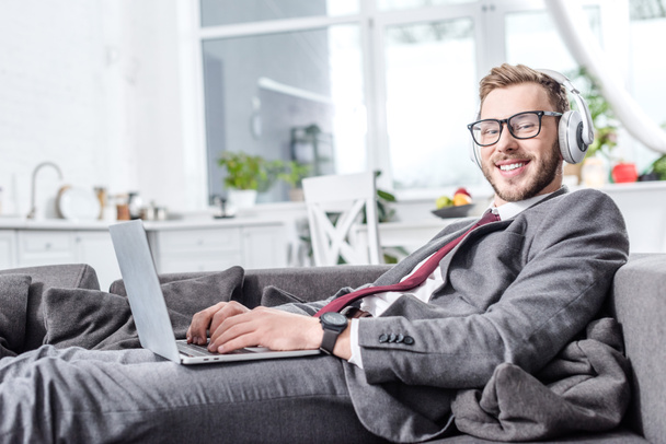 smiling businessman wearing headphones and using laptop on couch - Foto, immagini