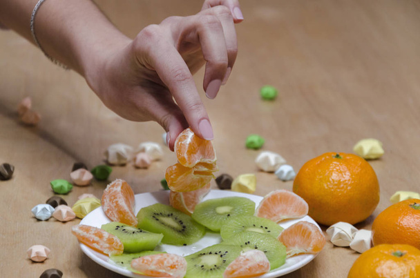 female hand with a slice of tangerines over a plate with fruit, against the background of the table, close-u - Fotografie, Obrázek
