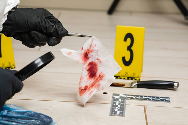 Ekspertem kryminologii patrzy przez szkło powiększające w krwawej serwetka na miejscu zbrodni. - Zdjęcie, obraz