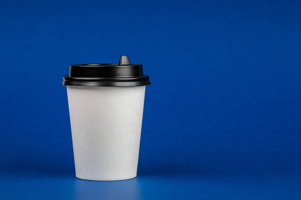 青の背景に黒のふた付きの紙のコーヒーのコンテナーです。テイクアウト飲料容器。あなたのデザインのドリンク カップ テンプレート - 写真・画像