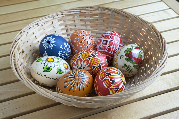Домашні розписані яйця ручної роботи в кошику, великодні прикраси на столі, маленька дерев'яна квітка
 - Фото, зображення