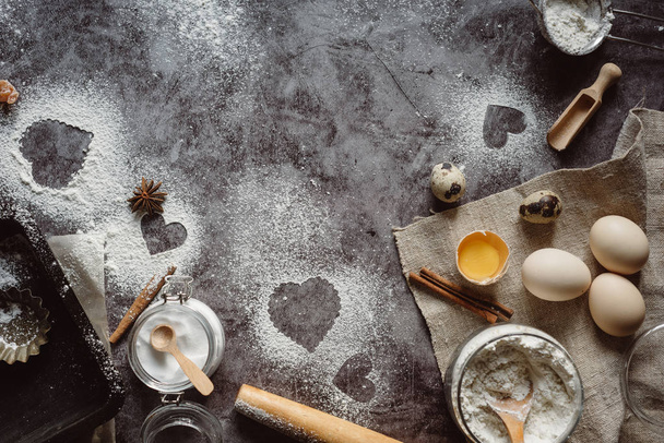 Healthy baking ingredients. Background with flour, rolling pin, eggs, and heart shape on kitchen gray kitchen table.  Top view for Valentines day cooking. Copy space. - Фото, зображення
