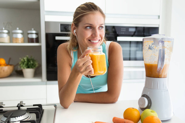 Shot of beautiful sporty young woman looking sideways and drinking vegetable detox juice in the kitchen at home. - Fotó, kép