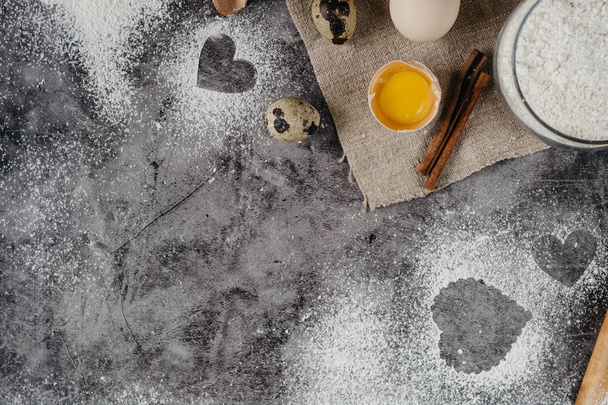 Healthy baking ingredients. Background with flour, rolling pin, eggs, and heart shape on kitchen gray kitchen table.  Top view for Valentines day cooking. Copy space. - Фото, зображення