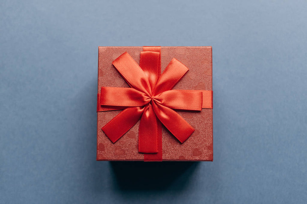 Caja roja con lazo con un regalo sobre fondo azul
 - Foto, imagen
