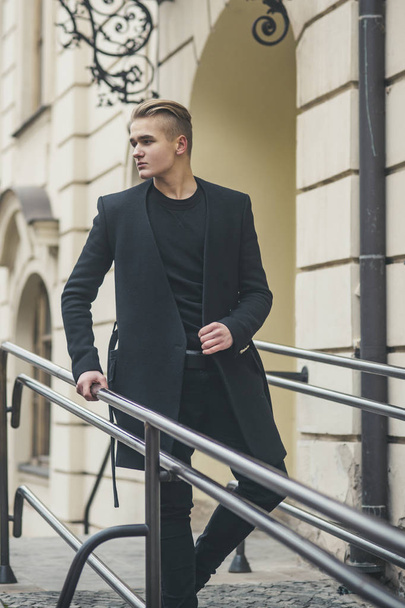 Young man in black outfit walks in old city. - 写真・画像