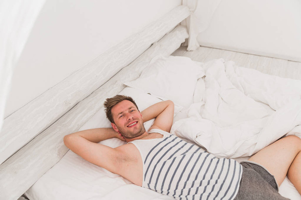 Happy young man lying on a bed indoor - Фото, изображение