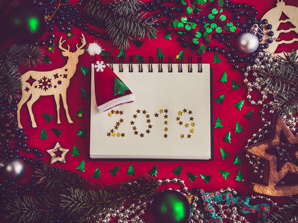 Colorful decorations, silver beads, Christmas tree branches, drawing and inscription in notebook on a red surface. Top view, close-up, flat lay. Happy New Year - Valokuva, kuva