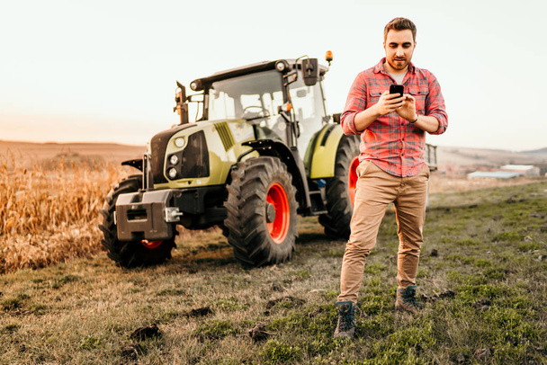 Farmer working and harvesting using smartphone in modern agriculture - tractor background - 写真・画像