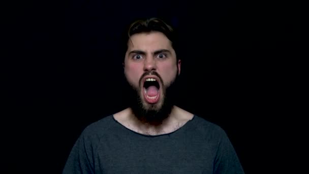 Портрет рыкающего красавца с бородой, стоящего и кричащего с большим открытым ртом, изолированного на черном фоне. Молодой сердитый бородатый мужчина кричит и кричит
 - Кадры, видео