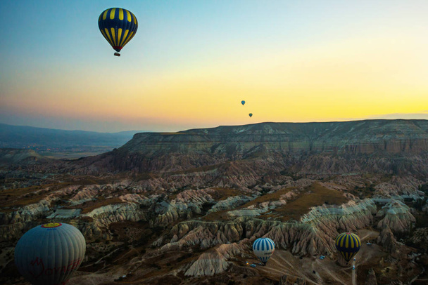 Cappadocia, Turkey: Cappadocia at sunrise - landscape with hot air balloons flying over mountain valley in sunlight and mist. Balloon against the blue sky in flight, colorful fun entertaining form of transport, flight in the air of the balloon, the c - Foto, Bild