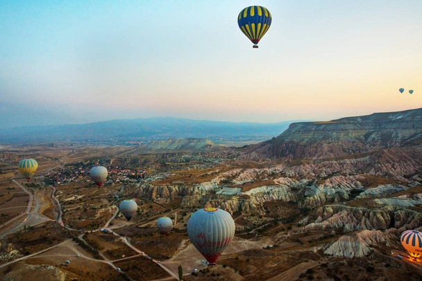 Cappadocia, Turkey: Cappadocia at sunrise - landscape with hot air balloons flying over mountain valley in sunlight and mist. Balloon against the blue sky in flight, colorful fun entertaining form of transport, flight in the air of the balloon, the c - Photo, Image