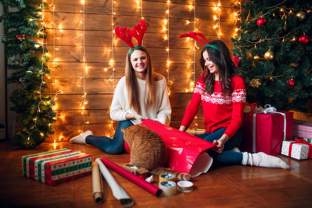 Friends wrapping and decorating gift near Christmas tree - Foto, imagen