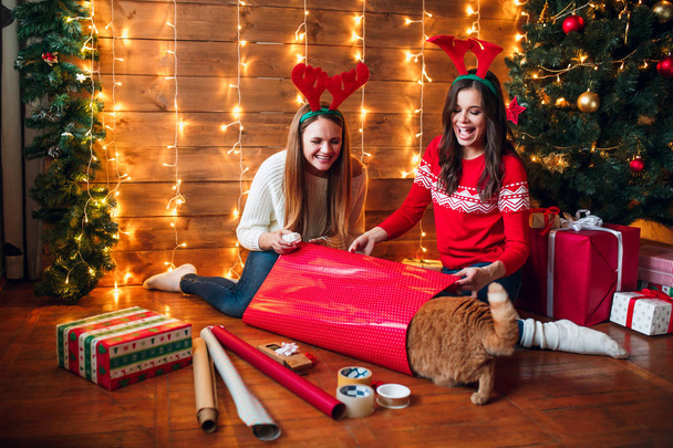 Friends wrapping and decorating gift near Christmas tree - Foto, imagen
