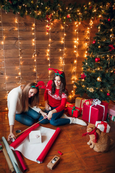 Friends wrapping and decorating gift near Christmas tree - Photo, image