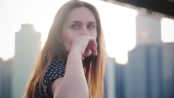 Close-up portrait of happy playful shy European woman with long hair smiling at camera at Manhattan city bridge skyline. - Materiaali, video