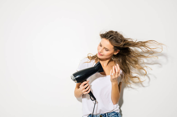 jovem mulher atraente soprando seu cabelo com secador de cabelo no fundo branco
 - Foto, Imagem