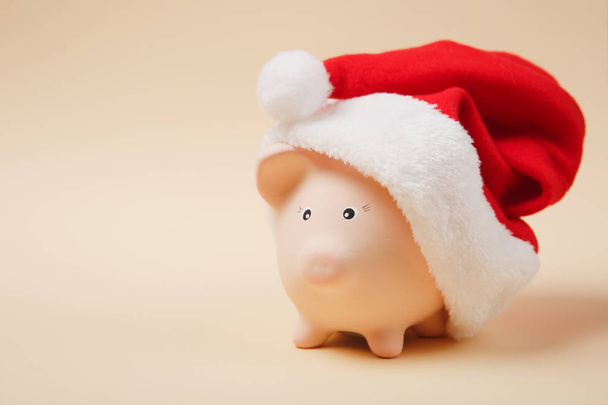 Close up of pink piggy money bank with Christmas hat isolated on pastel beige background. Money accumulation, investment, banking or business services, wealth concept. Copy space advertising mock up - Photo, image