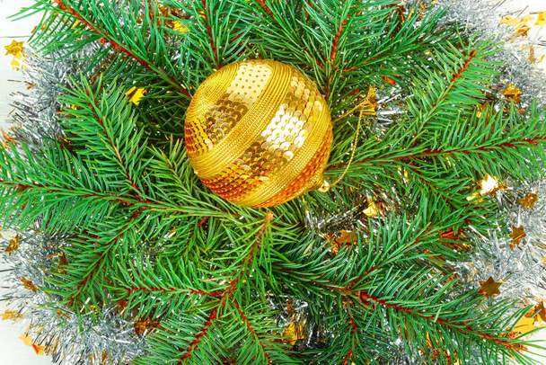 Christmas or New Year ornament. Bright golden ball on the background of a wreath of spruce twigs. Flat lay, top view. - Fotografie, Obrázek