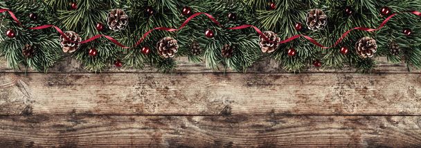 Creative layout frame made of Christmas fir branches, pine cones and red decoration on wooden background. Xmas and New Year theme. Flat lay, top view, wide composition - Photo, Image