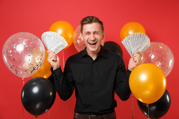 Jovem feliz em camisa clássica preta segurando lotes pacote de dólares em dinheiro em balões de ar fundo vermelho brilhante. Dia dos Namorados, Dia das Mulheres, Feliz Ano Novo, conceito de festa de aniversário mockup
 - Foto, Imagem
