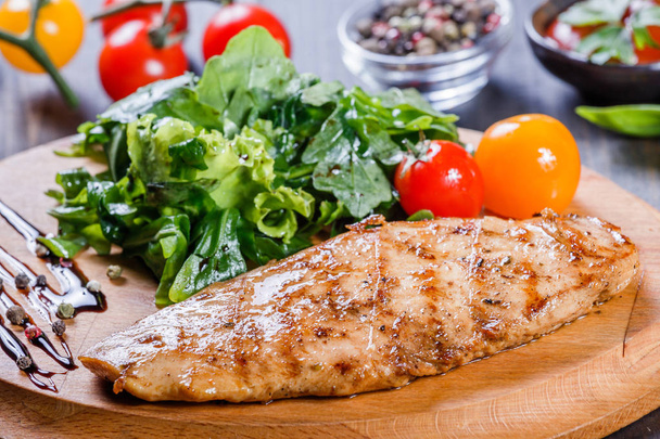 Grilled chicken fillet with fresh vegetable salad, tomatoes and sauce on wooden cutting board. Hot Meat Dishes. Top view - Photo, Image