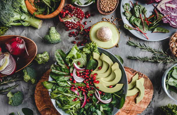 Здоровый свежий салат с авокадо, зеленью, рукколой, шпинатом, гранатом в тарелке на сером фоне. Здоровое веганское питание, чистое питание, диета, вид сверху
 - Фото, изображение