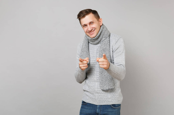 Handsome young man in gray sweater, scarf pointing index fingers on camera isolated on grey wall background. Healthy fashion lifestyle people sincere emotions, cold season concept. Mock up copy space - Photo, Image