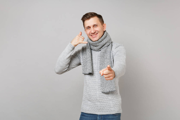 Handsome man in sweater, scarf doing phone gesture like says call me back, pointing index finger on camera isolated on grey background. Healthy lifestyle, people sincere emotions, cold season concept - Photo, Image