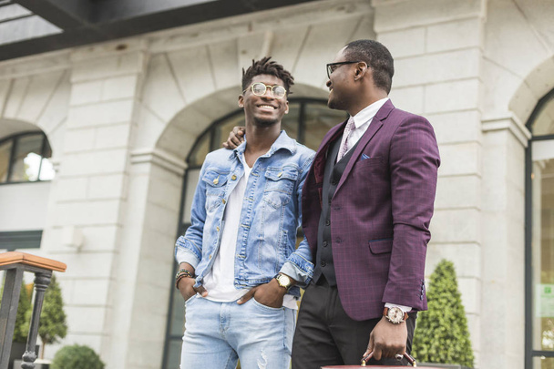 δύο νέοι και κομψό αφροαμερικάνων άνδρες στην πόλη χαμογελώντας και μιλώντας. σχέση πατέρα και ενήλικα γιο - Φωτογραφία, εικόνα