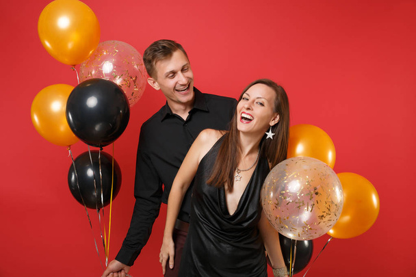 Impresionante pareja joven en ropa negra celebrando fiesta de cumpleaños aislada en globos de aire de fondo rojo brillante. San Valentín Día Internacional de la Mujer Feliz Año Nuevo 2019 concepto
. - Foto, imagen