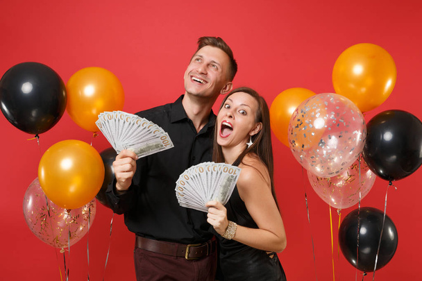 Couple in black clothes celebrating birthday holiday party, hold cash money isolated on bright red background air balloons. St. Valentine International Women Day Happy New Year 2019 concept. Mock up - Photo, Image