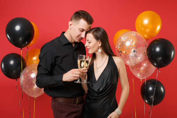 Impresionante pareja joven en ropa negra celebrando fiesta de cumpleaños aislada en globos de aire de fondo rojo brillante. San Valentín Día Internacional de la Mujer Feliz Año Nuevo 2019 concepto
. - Foto, Imagen